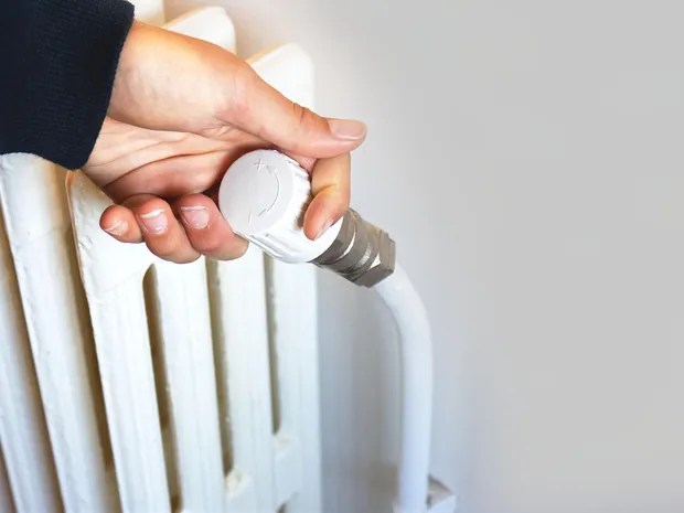 Hand stellt den Thermostatkopf am Heizkoerper ein