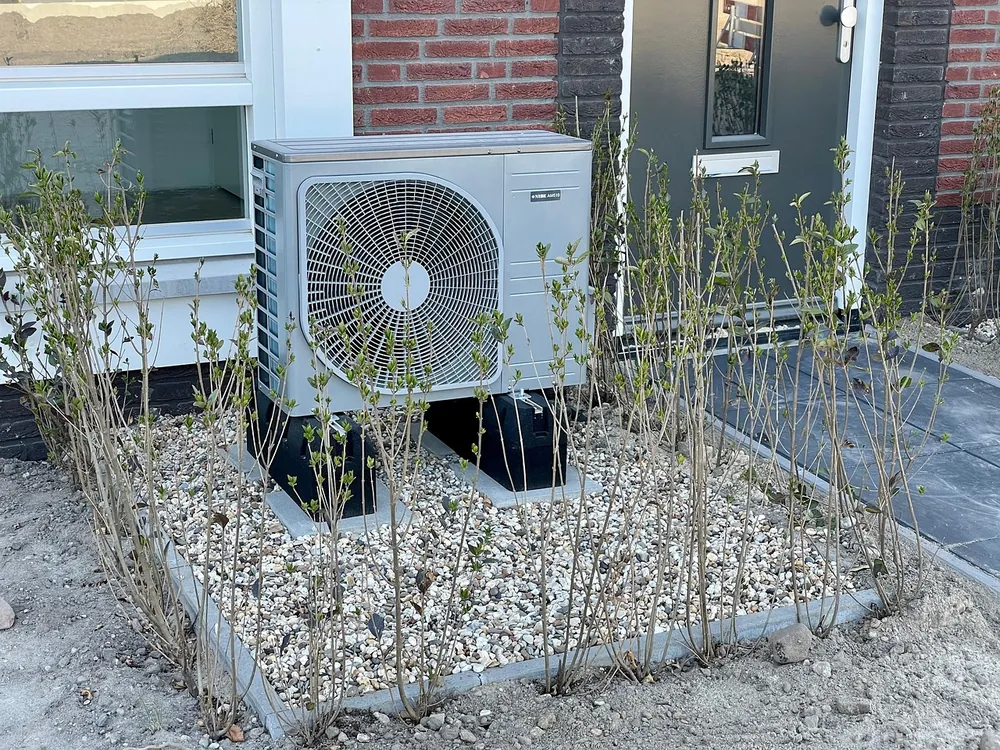 Aussengeraet einer Luftwaermepumpe neben einem Haus